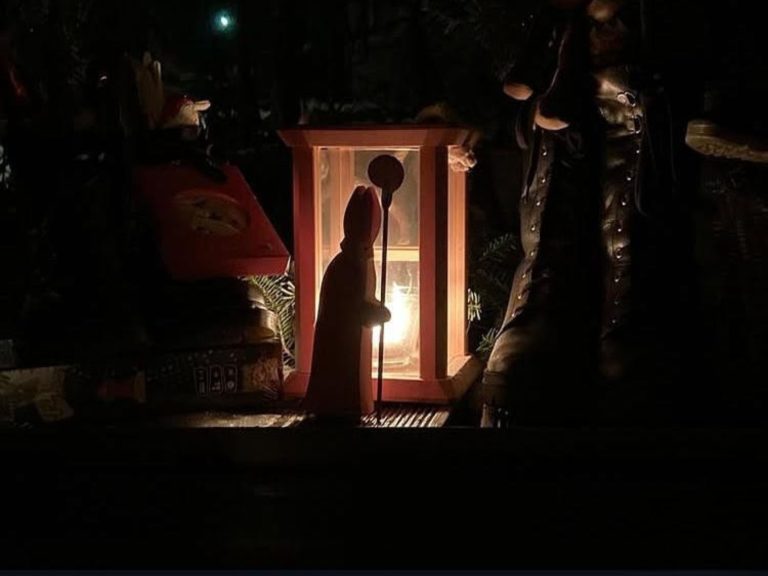 Eine Nikolausfigur vor einer Laterne im Dunkeln. Mit Süßigkeiten gefüllte Schuhe