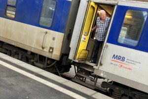 Ein Zug hält im Bahnhof. Ein Mann schaut aus der offenen Tür auf den Bahnsteig.