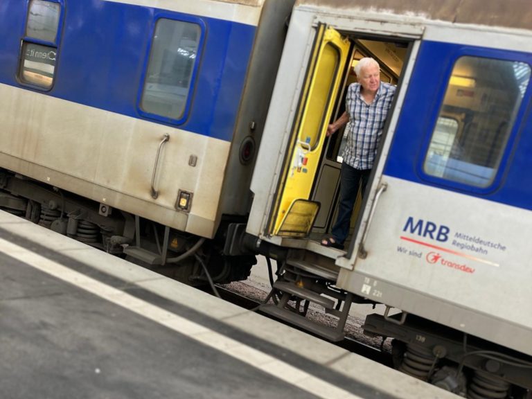 Ein Zug hält im Bahnhof. Ein Mann schaut aus der offenen Tür auf den Bahnsteig.